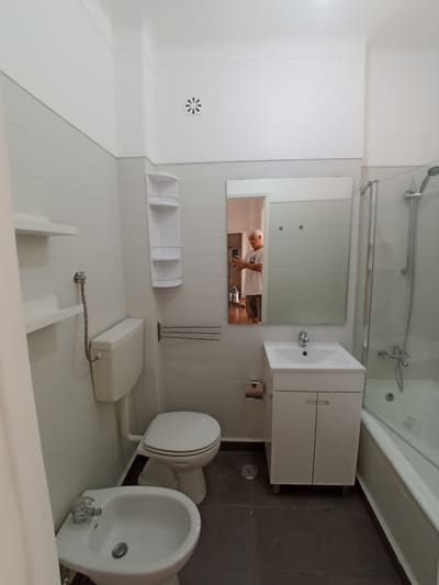 Casa de banho remodelada com resguardo de vidro, móvel suspenso e revestimento branco.