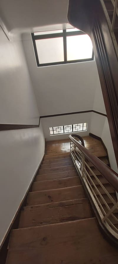 Caixa de escadas recuperada, com paredes brancas, corrimão em madeira e luz natural.