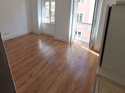 Pavimento novo em tom de madeira assente numa divisão remodelada, com rodapé e porta de sacada para a varanda.
